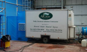 An All Clear Services-branded decontamination unit, connected to the blue sheeting of an asbestos removal enclosure.