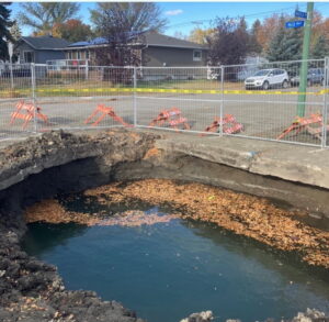 A burst water main has created a large hole in a suburban street, filled with water.